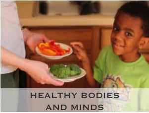 Photo of a child being offered a plate of red peppers or broccoli. The child is smiling and reaching for the red peppers. The overlaying text read: Healthy Bodies and Minds.