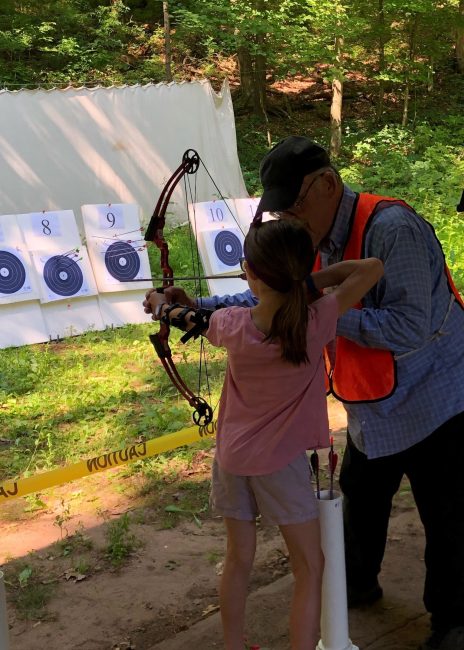 volunteer teaching a youth how to do archery