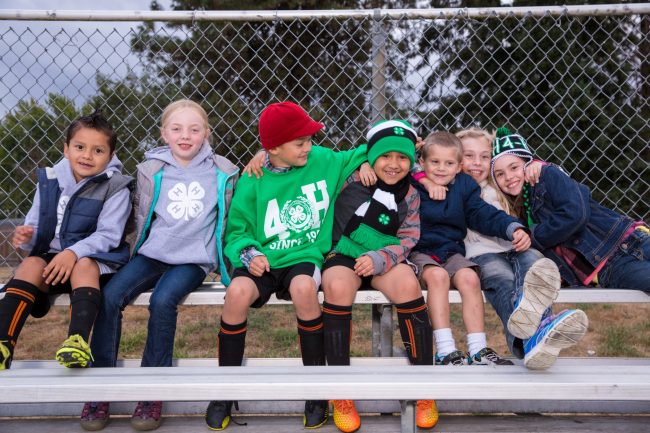 children sitting on a bench outside, wearing clothing with 4-H logos