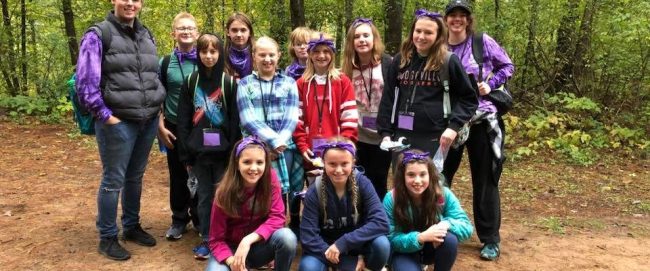 Middle school age children posing for a group photo in a wooded area
