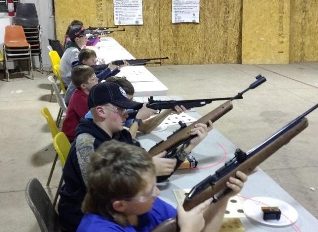 young people seated at tables with air rifles