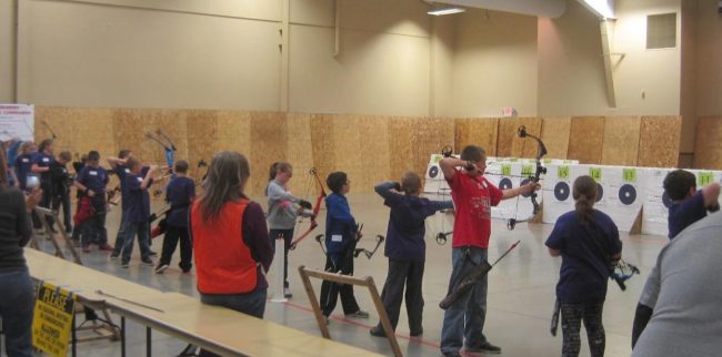 young people at an archery range, with some of them shooting a bow and arrow