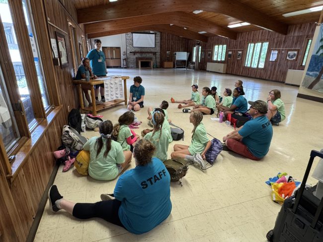 group of children and adults sitting on the floor listening to a speaker